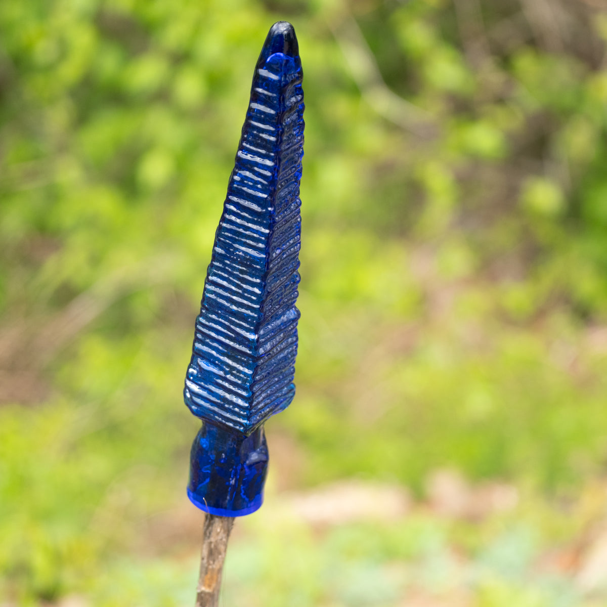 Blue glass arrowhead against a blurred green natural background