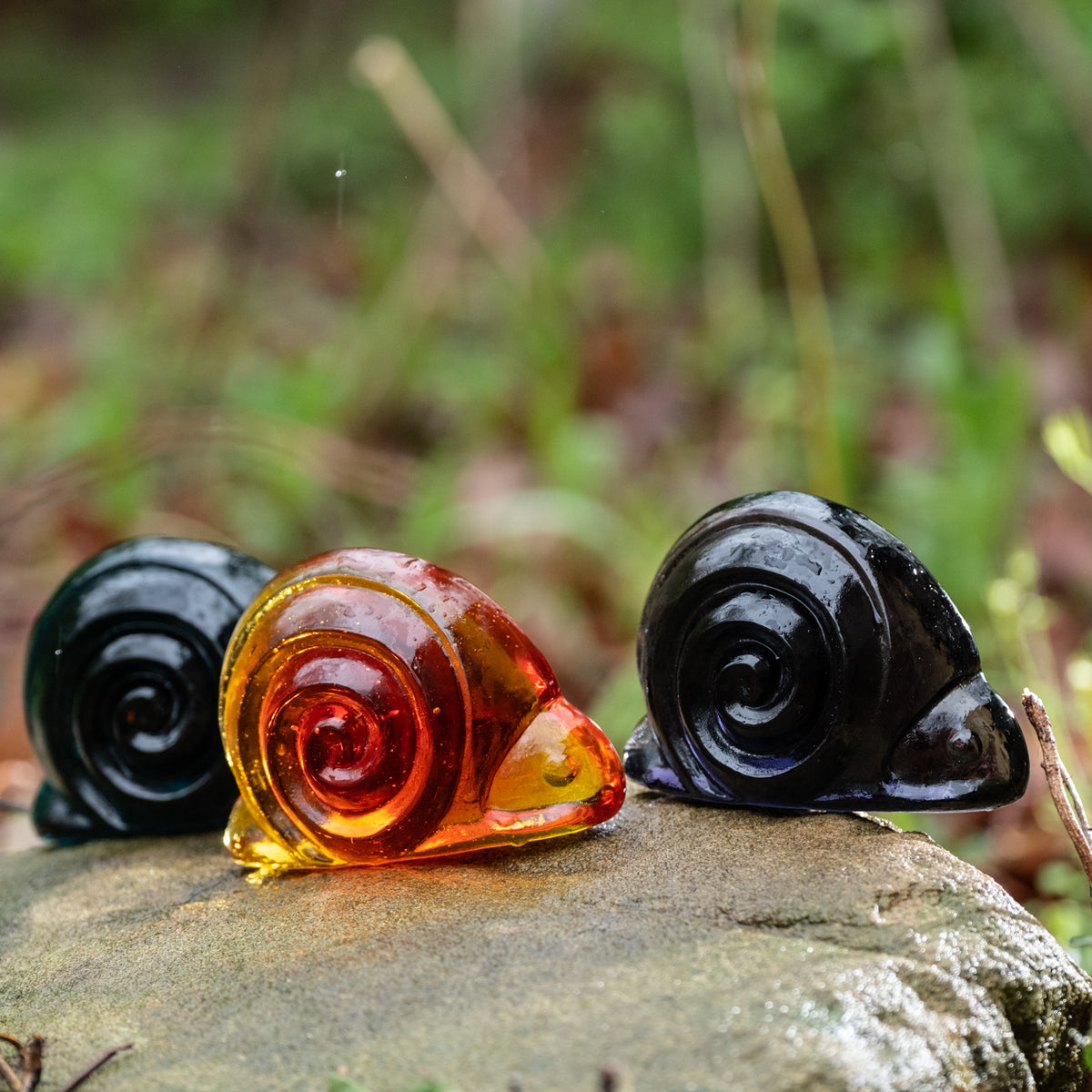 handcrafted glass snail figurines on a rock outside