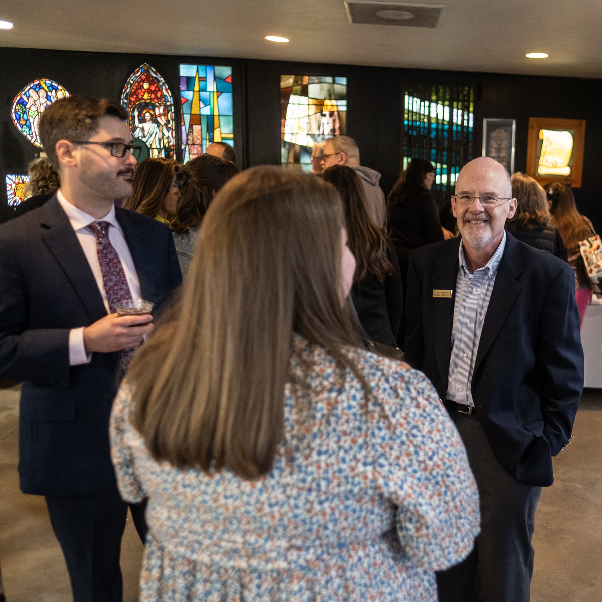 People socializing in a room with stained glass windows in the background