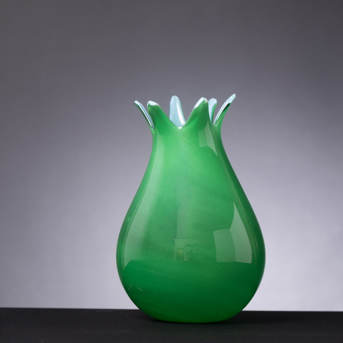 Green glass vase with a unique design on a gray background