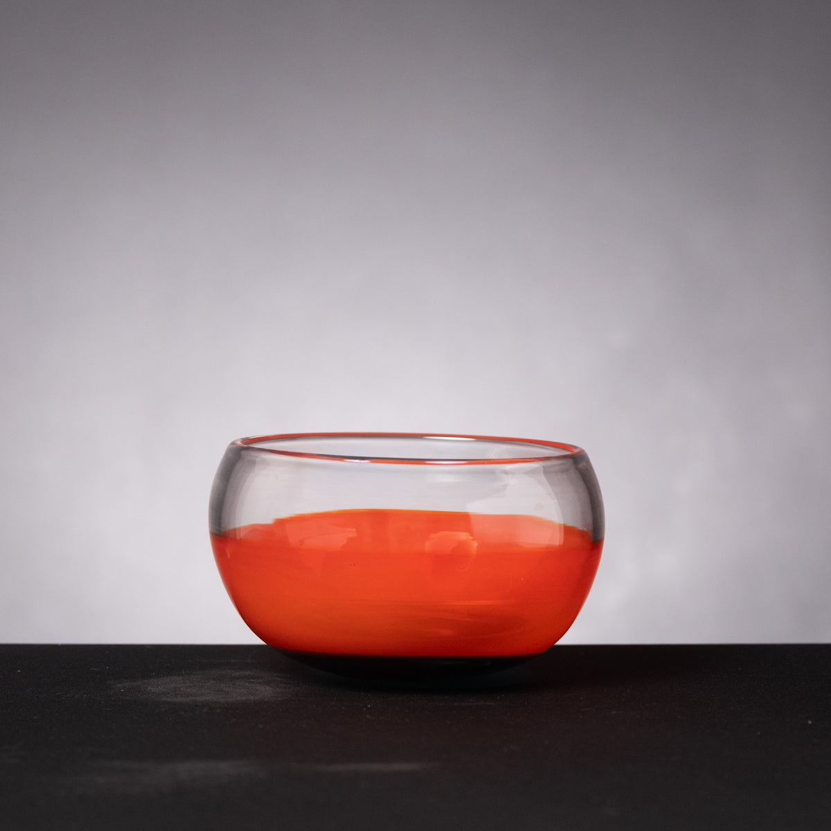 Clear glass bowl with red liquid on a dark surface and gray background
