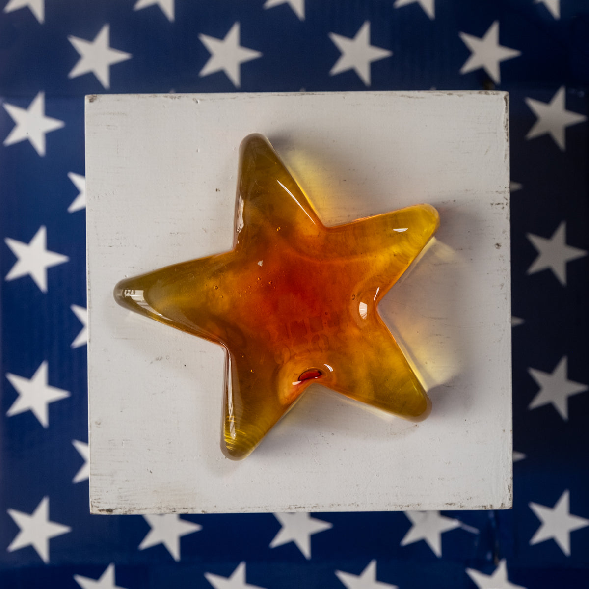 Star-shaped object with a gradient of colors on a white block against an American flag background