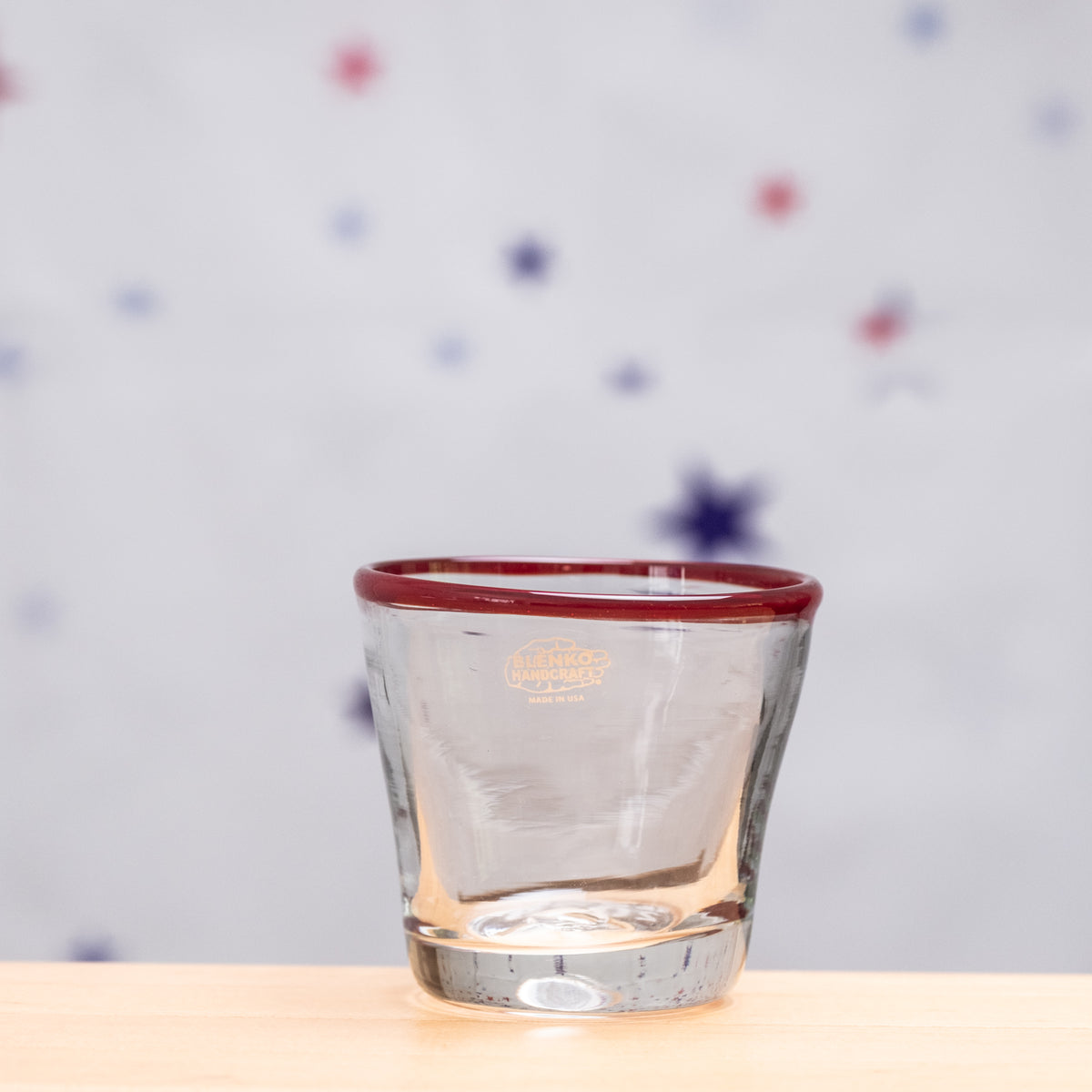 Clear glass with red rim on a light wooden surface and polka dot background