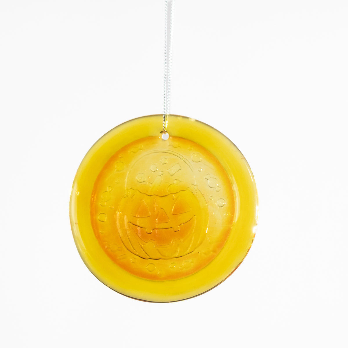 A round yellow glass ornament featuring an embossed jack-o'-lantern face, suspended by a white string against a plain white background.