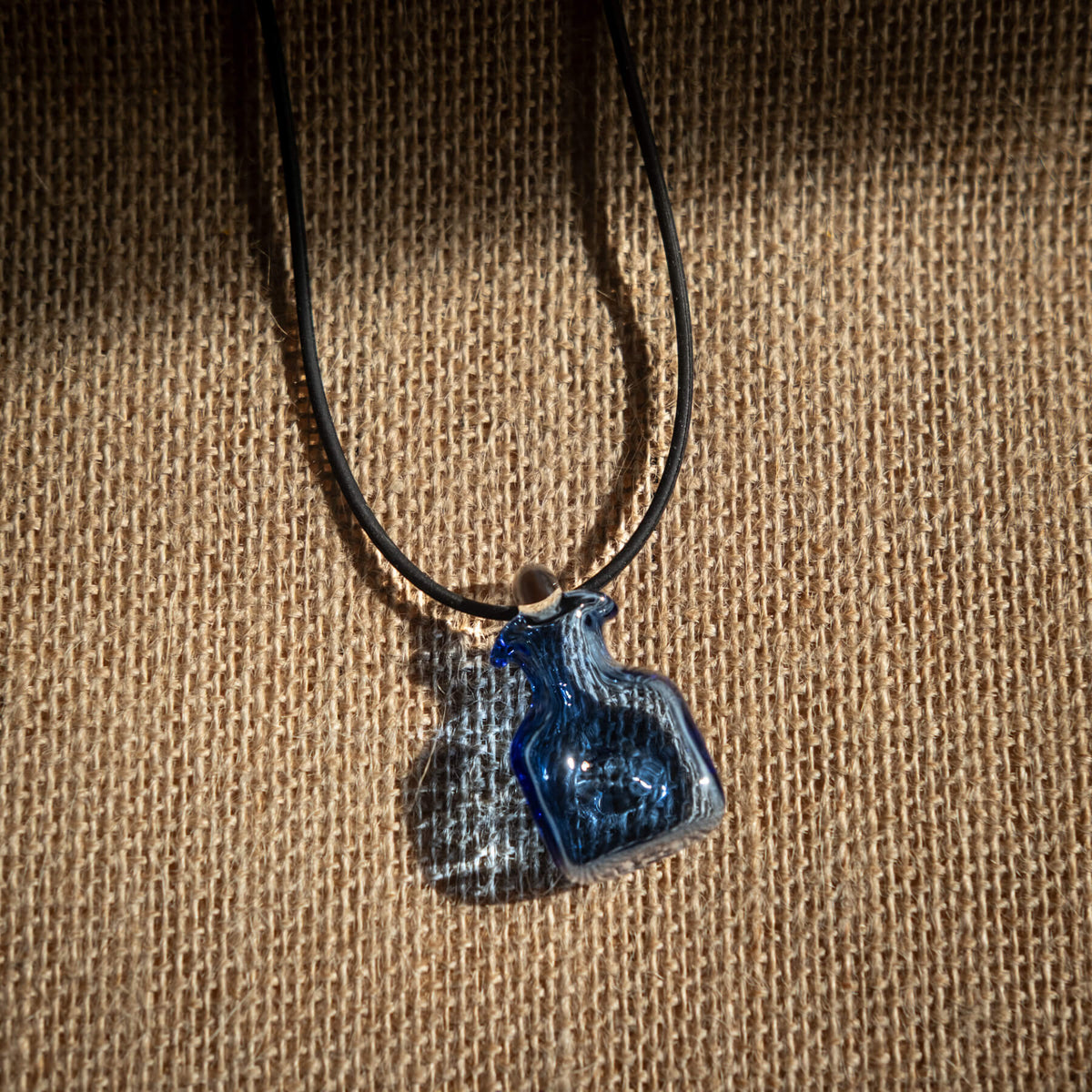 Blue glass pendant on a black cord against a brown fabric background