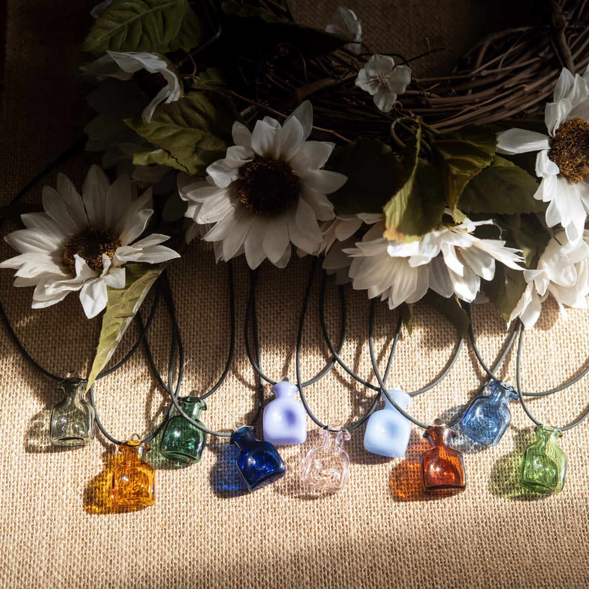 Colorful glass bottle necklaces on a textured surface with flowers in the background
