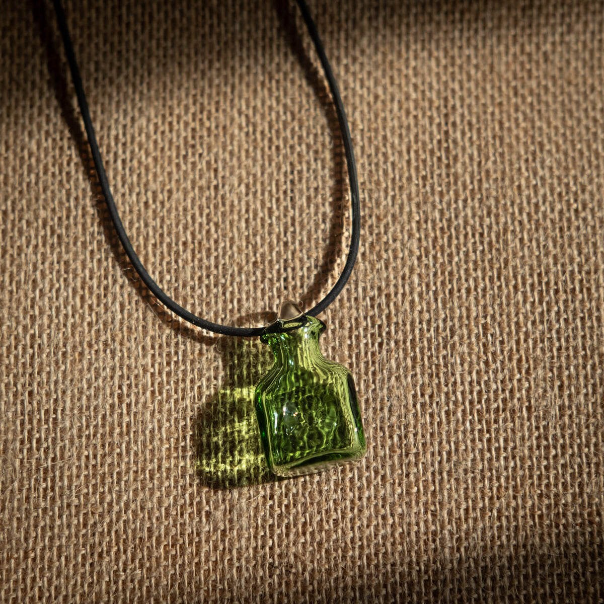 Green glass pendant on a black cord against a brown textured background