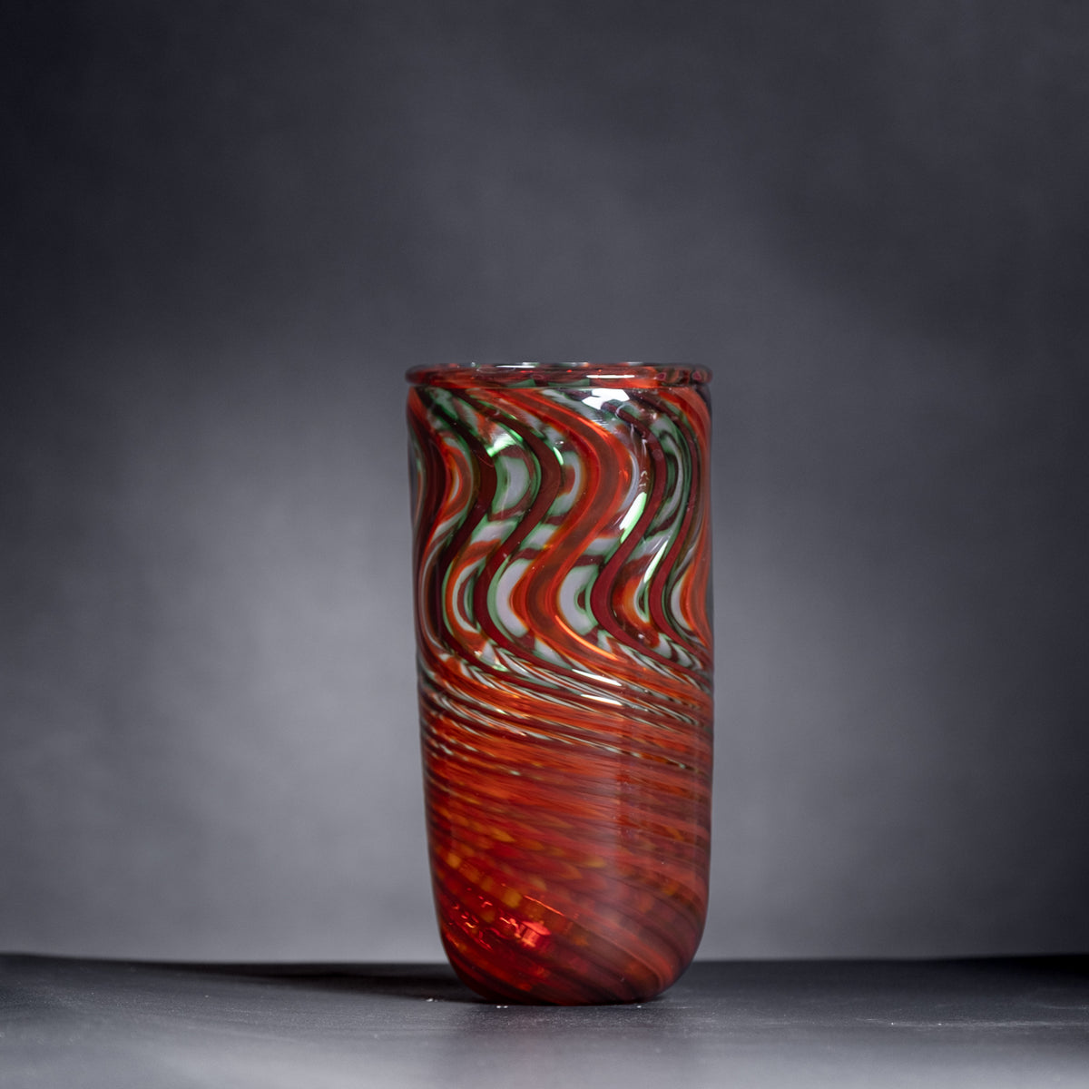 Glass vase with red and green swirl pattern on a dark background