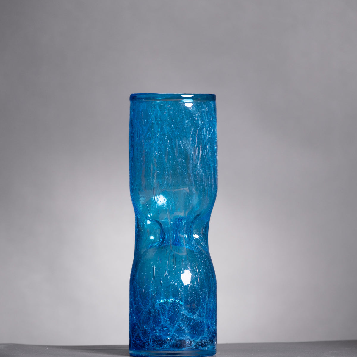 Blue glass vase with textured surface on a gray background