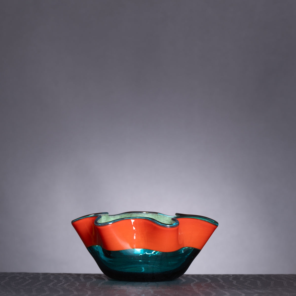 Glass bowl with wavy design in orange and blue on a dark surface with gray background