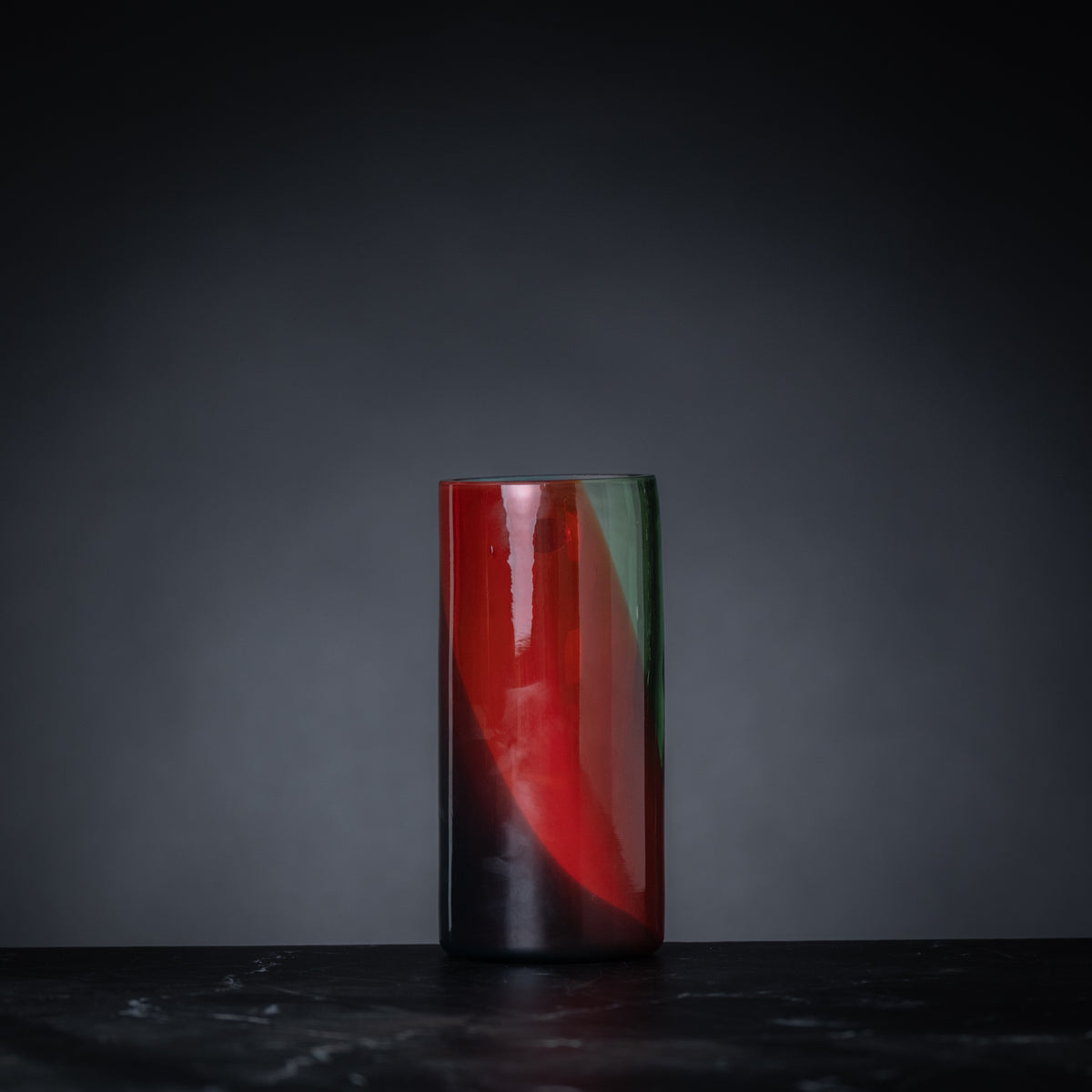 Cylindrical glass object with red interior on a dark surface and background
