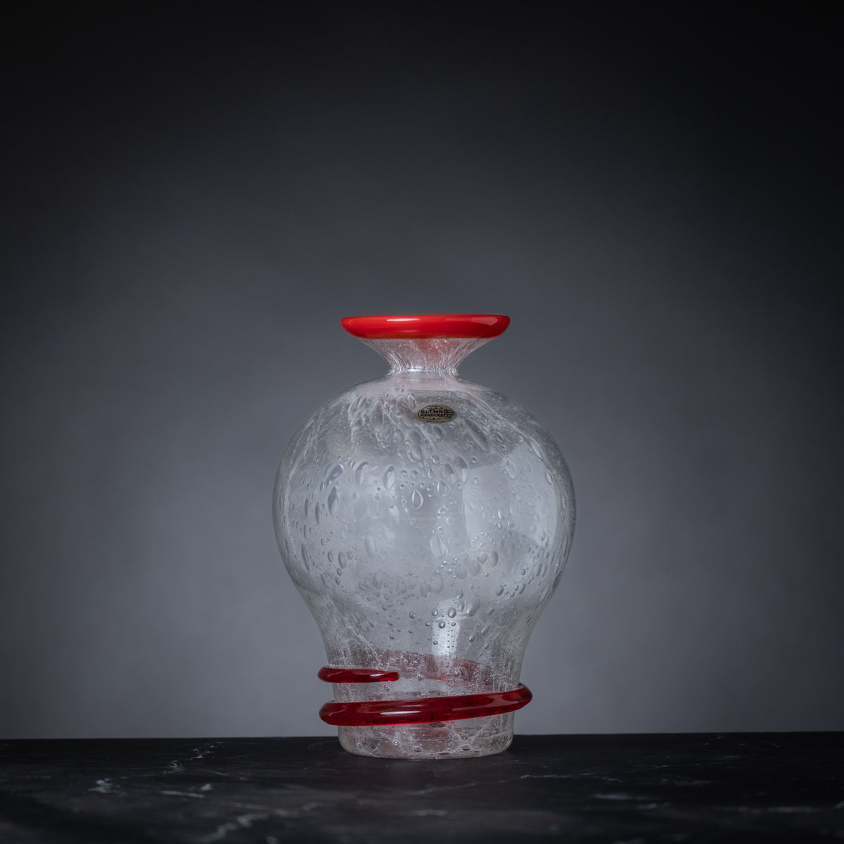 Glass vase with red accents on a dark surface and gray background