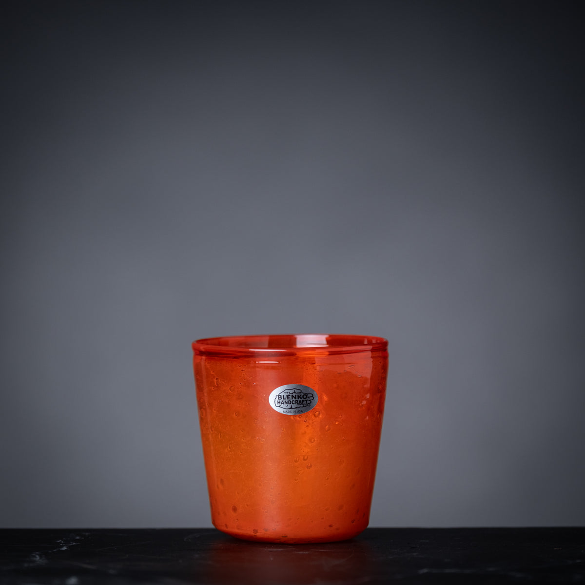 Red glass cup with a silver label on a dark surface and gray background
