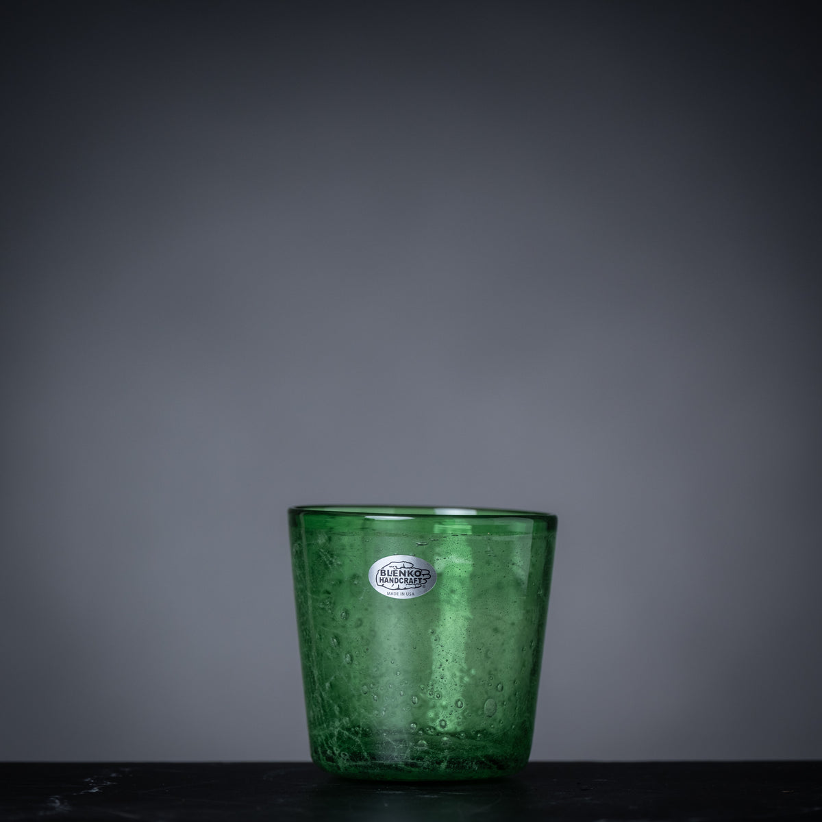 Green glass candle holder with a label on a dark surface and gray background