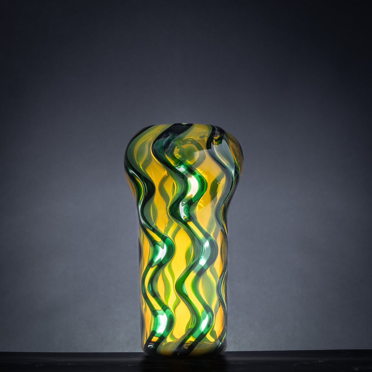 Glass vase with wavy design in green and yellow on a dark background