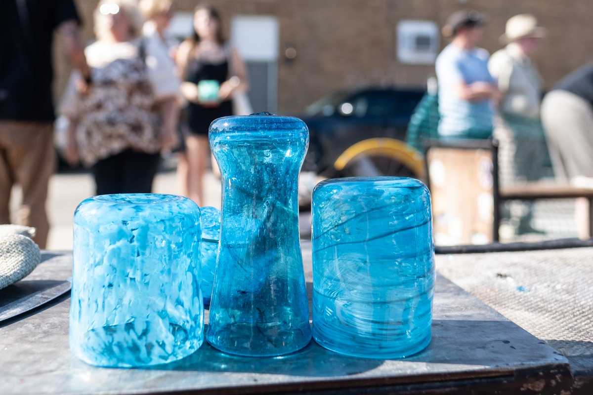 Three blue glass containers on a table with people and a bicycle in the background