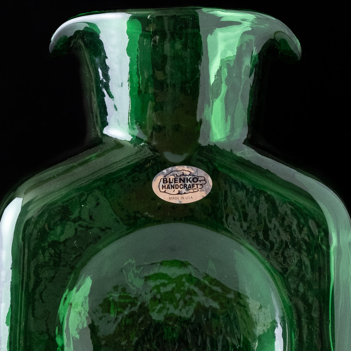 Green glass vase with a visible brand label on a black background