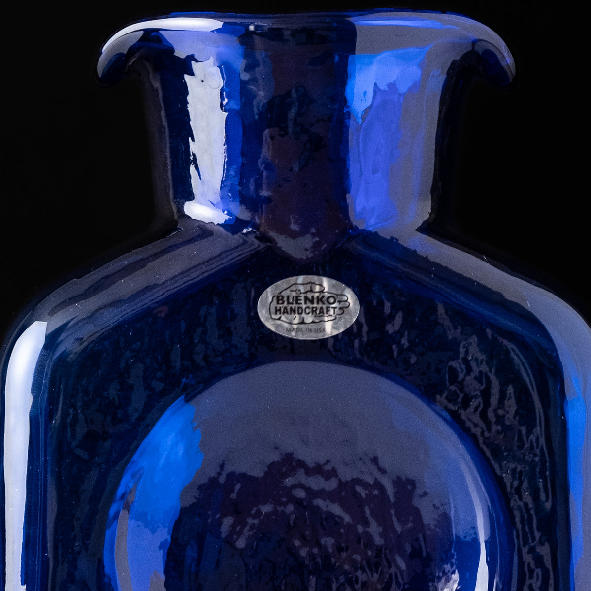 Blue glass vase with 'Buenko Handicrafts' label on a black background