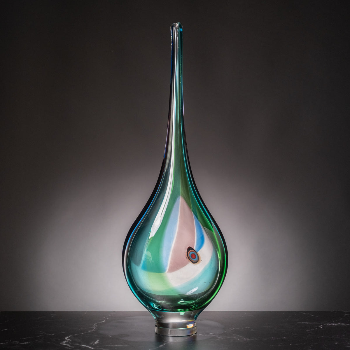 A hand-blown glass vase with a long, slender neck and a bulbous base, featuring iridescent swirls of teal, green, and pink on a dark gray gradient background.