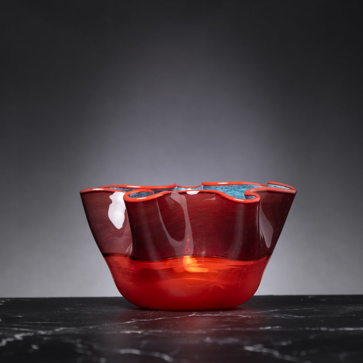 Red glass bowl with blue interior on a dark surface and gray background