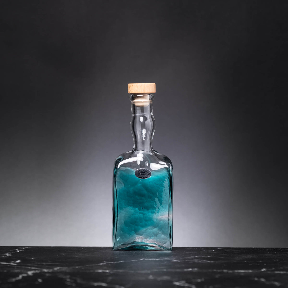Glass bottle with blue liquid and cork lid on a dark surface and background