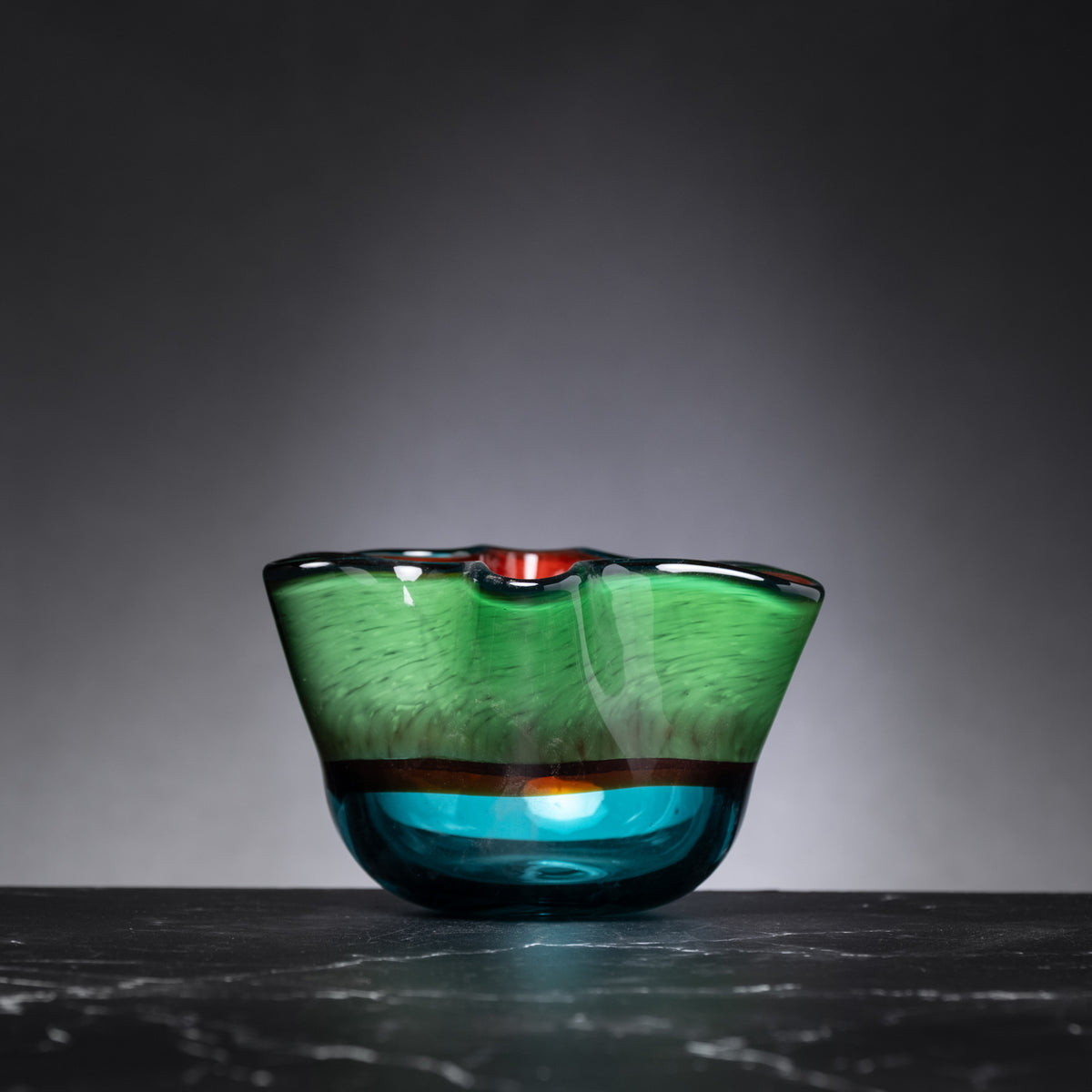 Glass bowl with green and blue gradient on a dark surface and gray background