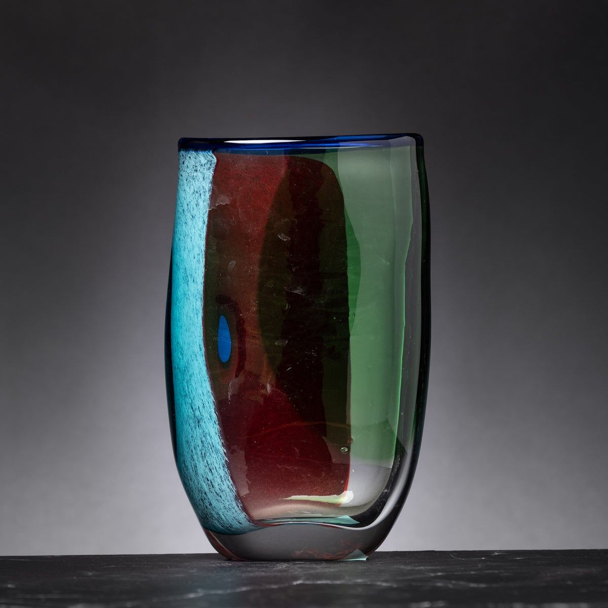 Colorful glass vase with blue, red, and green hues on a dark background