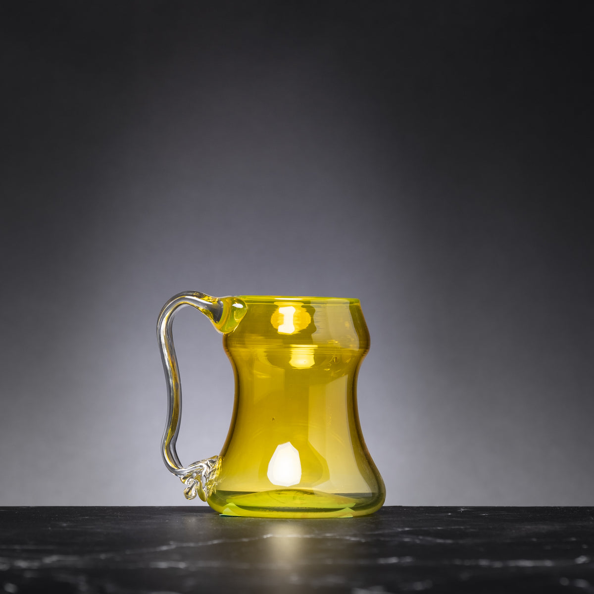Yellow glass mug on a dark surface with a gray background