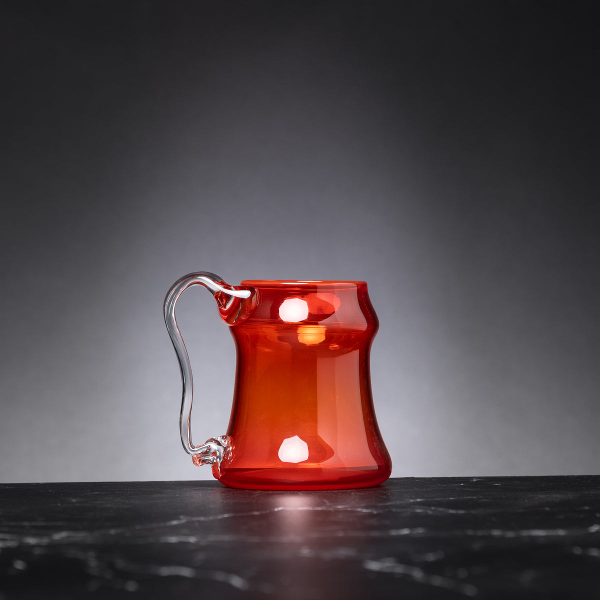 Red glass mug with a handle on a dark surface and gray background