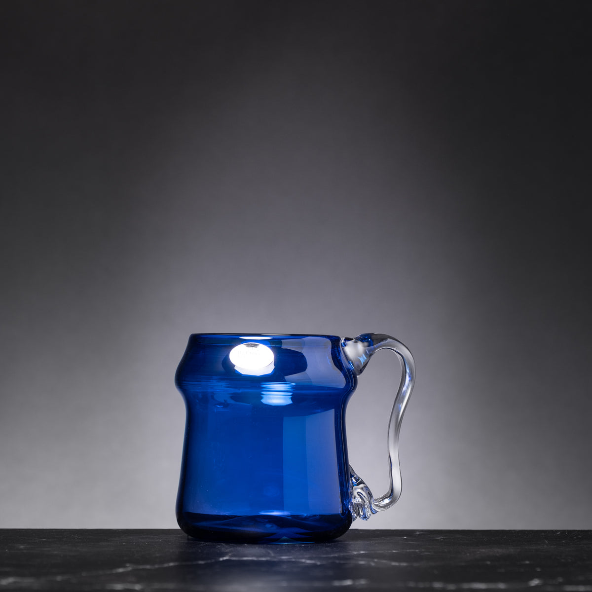 Blue glass mug on a dark surface with a gray background