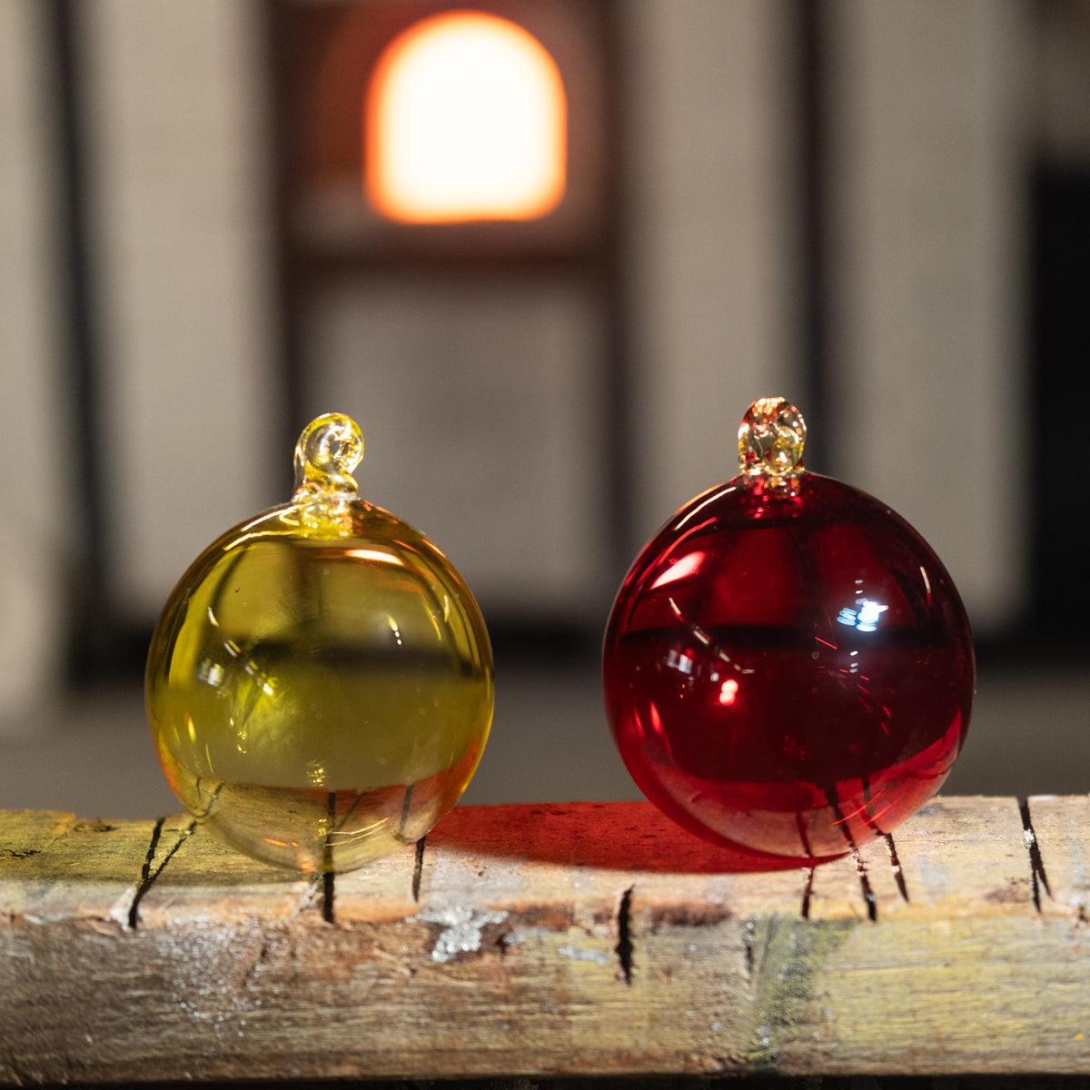 Two glass ornaments, one yellow and one red, on a wooden surface with a blurred background.